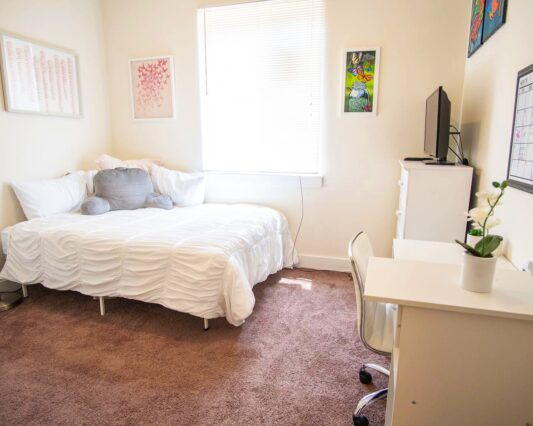 Student bedroom carpeted and decorated with furniture, pictures frames , and lamp